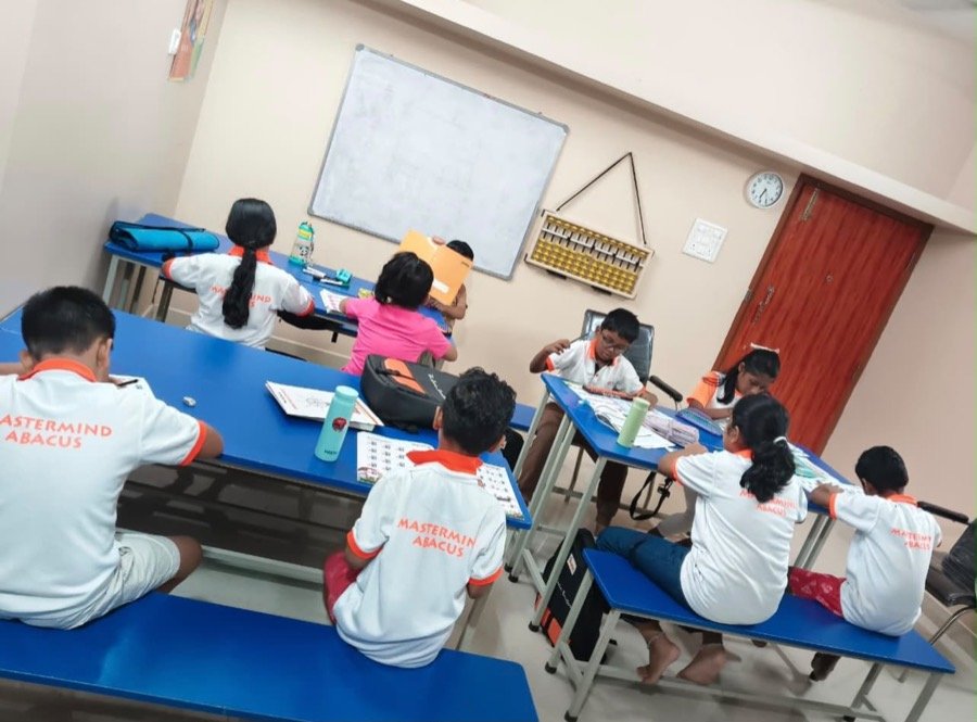 Students in Mastermind Abacus T-shirts working at their desks beside a large classroom abacus