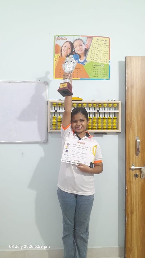 Abacus student raising her National Gala trophy while holding her certificate in the classroom